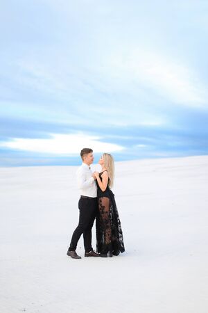Young man in white shirt hugging woman wearing black dress in winter steppe. Concept of winter photo session, relationship and love, happy couple.の写真素材