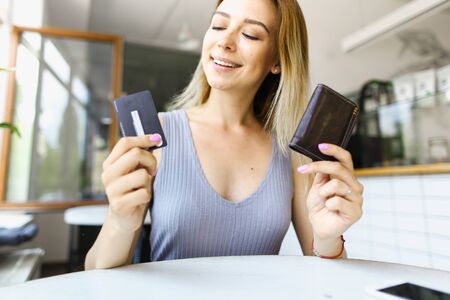 Blonde girl sitting at cafe and keeping wallet. Concept of paying by credit card.の写真素材