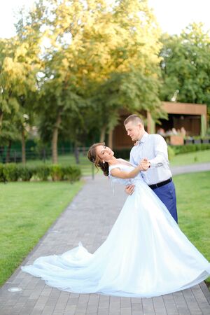 Young fiancee dancing with groom in park and wearing white dress. Concept of wedding and bridal photo session.の写真素材