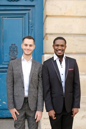 Two boys, caucasian and afro american, wearing suits standing near building. Concept of fashion and businessmen.の写真素材