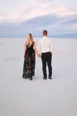 Back view of man and blonde girl wearing black dress walking in snowed white steppe. Concept of relationaship nad winter photo session.の写真素材