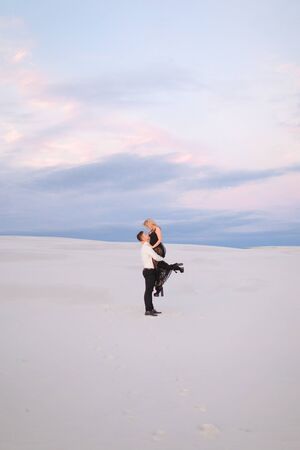 Young man holding womn wearing blakc dress in snowed field. Concept of love and winter photo session.の写真素材