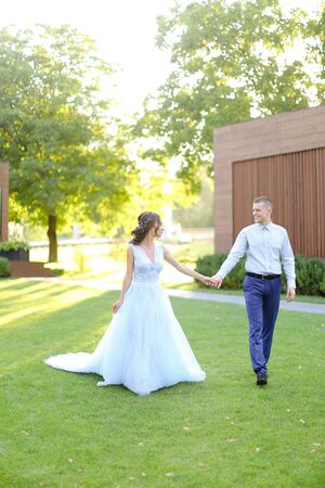Caucasian nice bride walking in park with groom, wearing white amazing dress. Concept of wedding and bridal photo session in open air.の写真素材