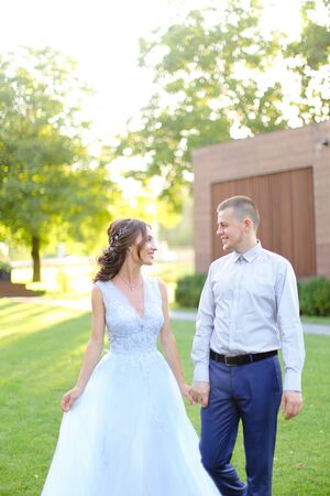 Caucasian beautiful bride walking in park with groom, wearing white amazing dress. Concept of wedding and bridal photo session in open air.の写真素材