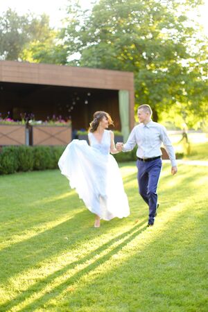 Cacuasian bride walking with groom in park and holding hands, wearing white dress. Concept of wedding and bridal photo session in open air.の写真素材
