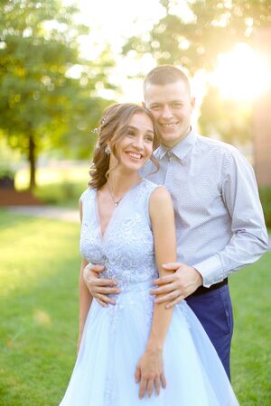 Happy smiling groom hugging fiancee in park, sun rays. Concept of bridal couple and wedding photo session in open air.の写真素材