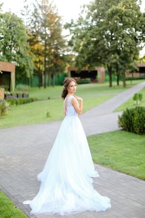 Caucasian beautiful fiancee standing in garden and wearing long white dress. Concept of bridal vogue and fashionable bride.の写真素材