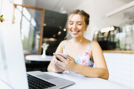 Young girl typing on smartphone and surfing internet by laptop at cafe. Concept of purchasing things online and modern technology.の写真素材