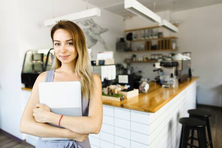 Blonde housewife standing with laptop in kitchen and smiling. Concept of happy wife and modern technology.の写真素材