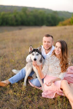 Young pretty woman and man sitting on gras with malamute. Concept of relatonship, picnic and dog.の写真素材