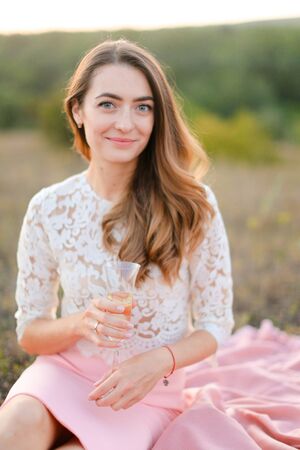 Young pretty woman sitting on pink plaid in field. Concept of beauty and picnic on nature.の写真素材
