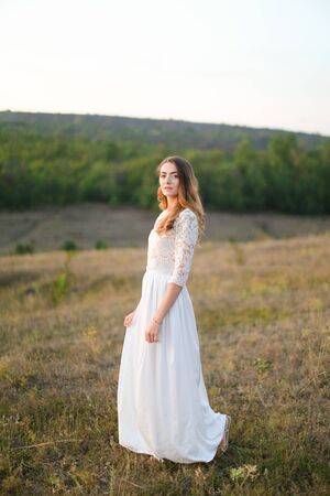 Caucasian pretty fiancee standing in steppe and wearing white dress. Concept of nature, bridal photo session on nature and beauty.の写真素材