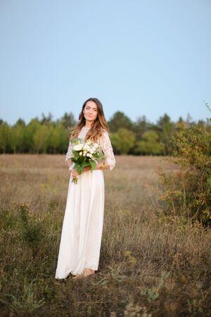 Caucasian fiancee with white bouquet background in steppe background. Concept of bridal photo session on nature and floristic art.の写真素材