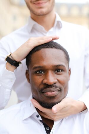 Caucasian man holding afro american guy head by hands.の写真素材