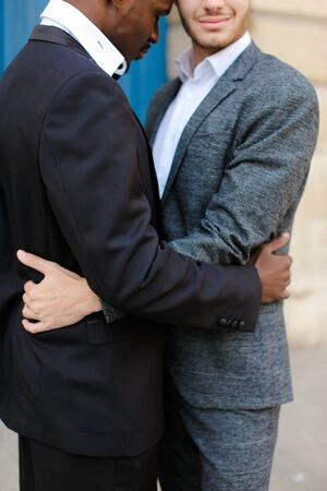 Afro american happy man hugging caucasian guy in door background, wearing suit. Concept of same sex couple and gays.の写真素材