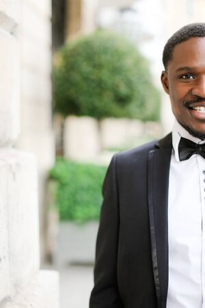 Portrait of afro american smiling man wearing dark suit and standing outdoors. Concept of black businessman.の写真素材
