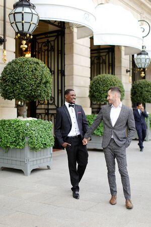 Afro american and caucasian happy gays walking outside and holding hands in city. Concept of same sex male couple.の写真素材