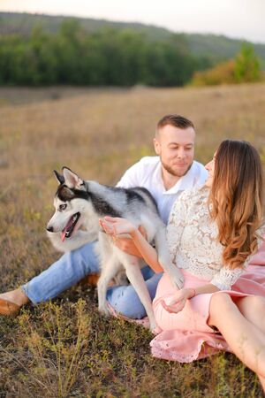 Young caucasian woman and man sitting on gras with malamute. Concept of relatonship, picnic and dog.の写真素材