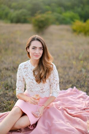Young happy woman sitting on pink plaid in field. Concept of beauty and picnic on nature.の写真素材