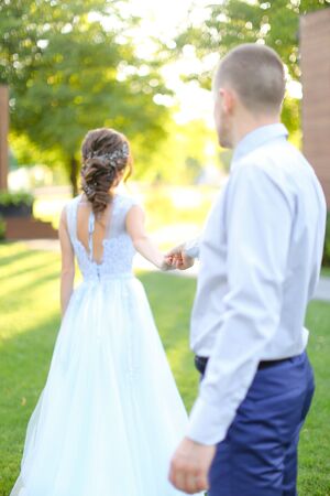 Groom following bride and walking in park holding hands. concept of wedding and bridal photo session in open air.の写真素材