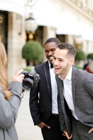 Afro american and caucasian men standing near female photographer with camera. Conceptof gay photo session and business.の写真素材