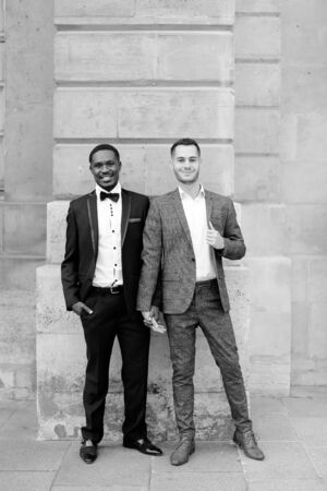 Black and white photo afro american and caucasian happy gays standing near building and wearing suits. Concept of lgbt and walking in city.の写真素材