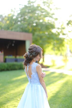 Back view of caucasian fiancee walking in garden. oncept of bridal hair do and wedding photo session on nature.の写真素材
