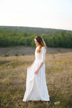 Caucasian young fiancee standing in steppe and wearing white dress. Concept of nature, bridal photo session on nature and beauty.の写真素材