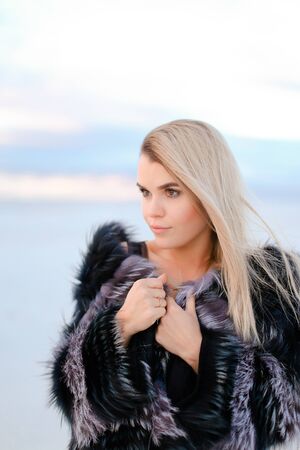 Caucasian blonde woman wearing black transparent dress standing on snowed background. Concept of winter photo session an fashion.の写真素材