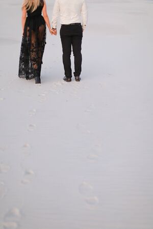 Back view of man and girl wearing black dress walking in snowed white steppe. Concept of relationaship nad winter photo session.の写真素材
