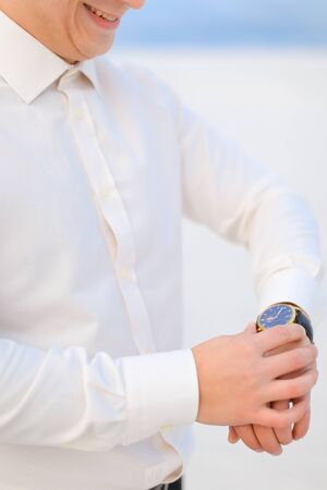 Close up young smiling male person standing in winter steppe and looking at watch. Concept of waiting and seasonal photo session.の写真素材