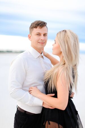 Young handsome husband in white shirt hugging wife wearing black dress in winter steppe. Concept of winter photo session, relationship and love, happy couple.の写真素材