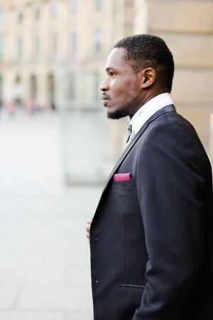 Portrait of afro american happy man wearing dark suit and standing outside. Concept of black businessman.の写真素材