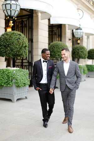 Afro american and caucasian happy handsome gays walking outside in city. Concept of same sex male couple.の写真素材