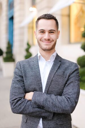 Portrait of happy young caucasian man wearing grey suit outside. Concept of successful businessman and male fashion.の写真素材