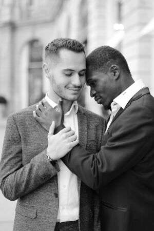 Black and white photo of afro american gay hugging caucasian boy outside, wearing suits. Concept of lgbt and same sex couple.の写真素材