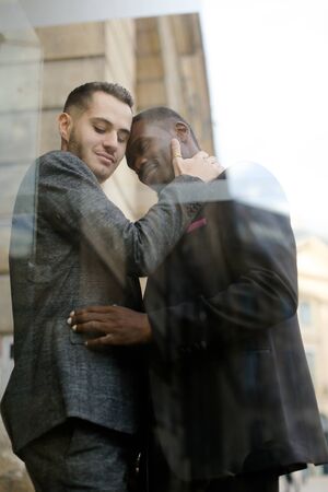 Reflection in window of two hugging men, afro american and caucasian. Concept of gays and lgbt.の写真素材