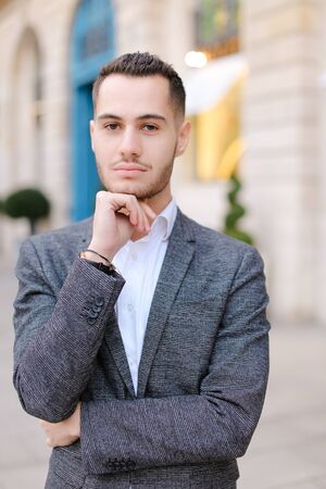 Portrait of young cacuasian handsome male person wearing suit standing near building outdoors. Concept of fashion and businessman, urban life.の写真素材