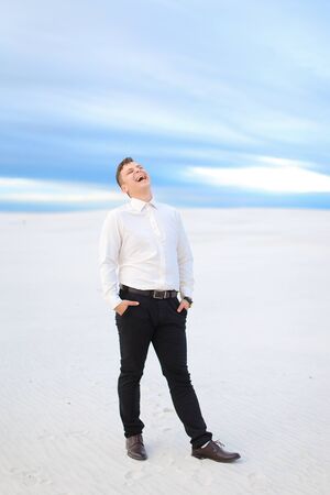 Young happy male person standing in winter steppe and wearing white shirt, snow in backgrounf. Concept of seasonal photo session.の写真素材