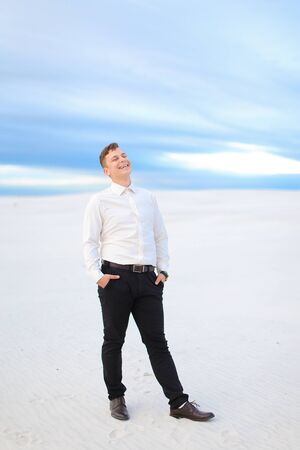 Young handsome male person standing in winter steppe and wearing white shirt, snow in backgrounf. Concept of seasonal photo session.の写真素材