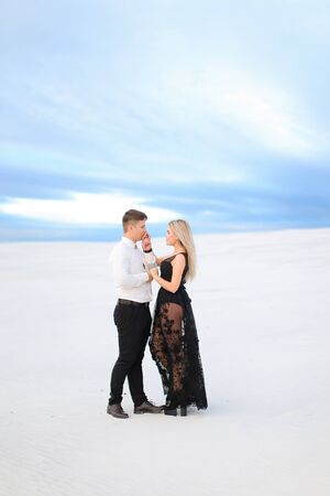 Young male person in white shirt hugging woman wearing black dress in winter steppe. Concept of winter photo session, relationship and love, happy couple.の写真素材