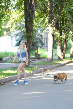 Young beautiful woman girl lady blond hair with red lips in casual style american bulldog. Woman plays with dog glad, laughing, happy and inspired walking goes.の写真素材