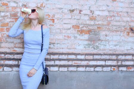 Woman blond hair slim athletic figure near brick wall stands wearing sunglasses.の写真素材