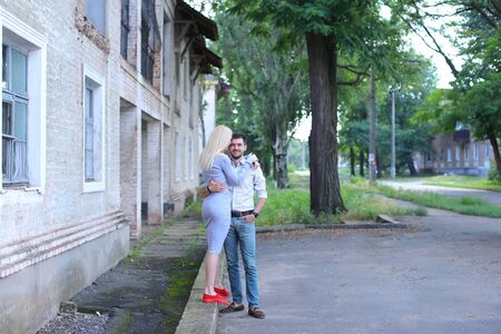 Girlfriend and boyfriend standing next to each other, posing, talking and laughing, hugging on street. Girl dressed in midi gray dress and red slip-on, guy straight, keeping hands in pants pockets and looking directly into camera, he dressed in blue jeans and white striped shirt. Concept of young couple in love, long-awaited meeting, love will save world, family, lovestory shooting.の写真素材