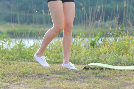 Photo slender legs girl in black shorts and white sneakers near gymnastic mats in woods on background of river. Concept of fitness, slim figure, healthy lifestyle, activity, good physical fitness, classes in nature.の写真素材