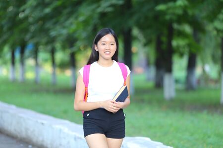 Girl female teenager with black hair in a bob white east Asian woman green park with a backpack background. Lady walking, goes, walk away, look at the camera.の写真素材