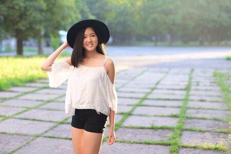 female nature keeps his hat summer sun sunset looks pleased. azitka woman black hair white shirt black shorts dancing around the trees looking at the camera. portrait. spinningの写真素材