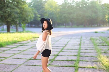 female nature keeps his hat summer sun sunset looks pleased. azitka woman black hair white shirt black shorts dancing around the trees looking at the camera. portrait. spinningの写真素材