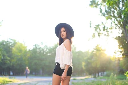 female hat nature summer sun sunset looks pleased. azitka woman black hair white shirt black shorts dancing around the trees looking at the camera. portrait.の写真素材