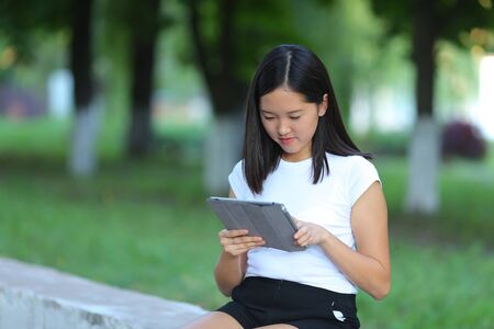 Girl female teenager with black hair in a bob white east Asian woman green park background. Lady holding plate and presses a finger, smiling, looking into the camera.の写真素材
